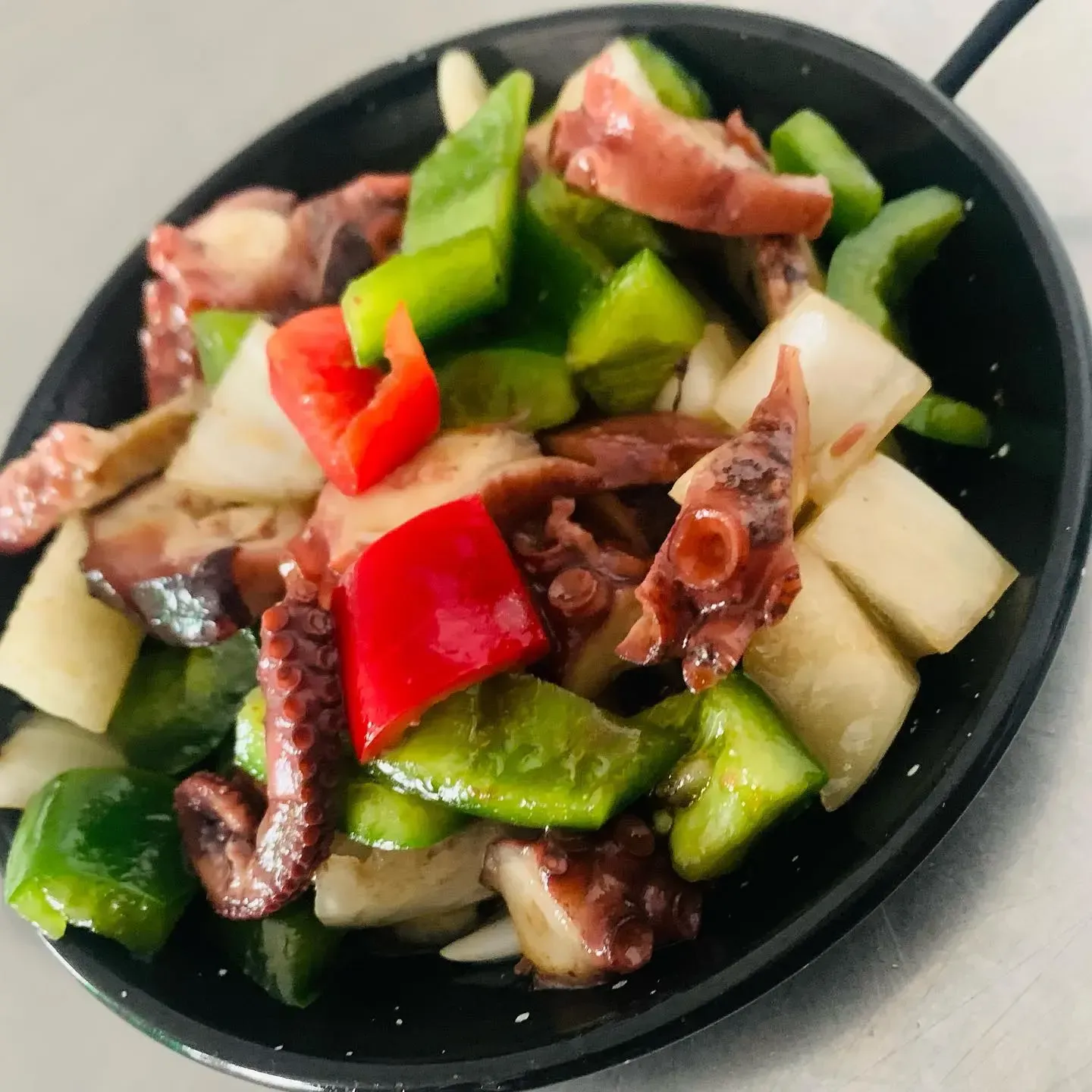 Bol negro de ensalada de pulpo con pepino verde y trozos de pimiento rojo.