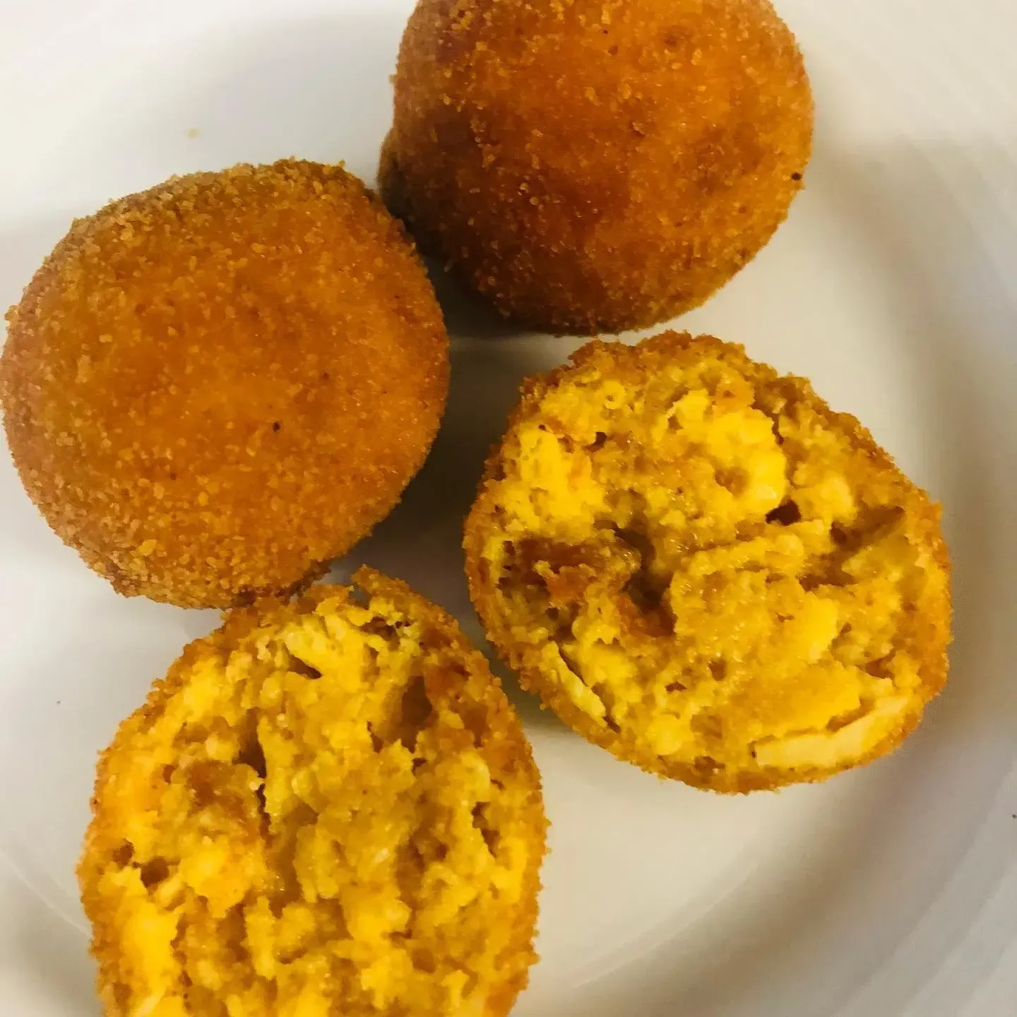 Tres bolas fritas de color marrón dorado, dos de ellas cortadas para mostrar un relleno amarillo sobre un plato blanco.