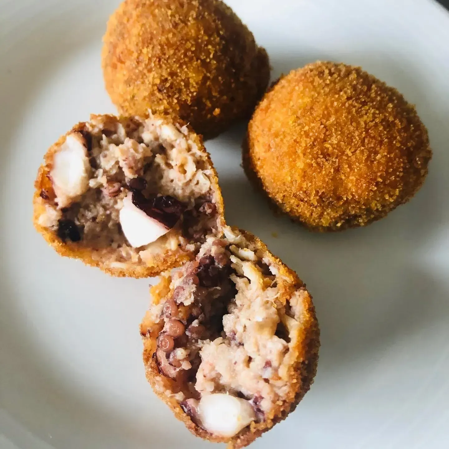 Tres bolas empanadas y fritas en un plato, dos de ellas cortadas por la mitad dejando ver un relleno de chocolate y crema.