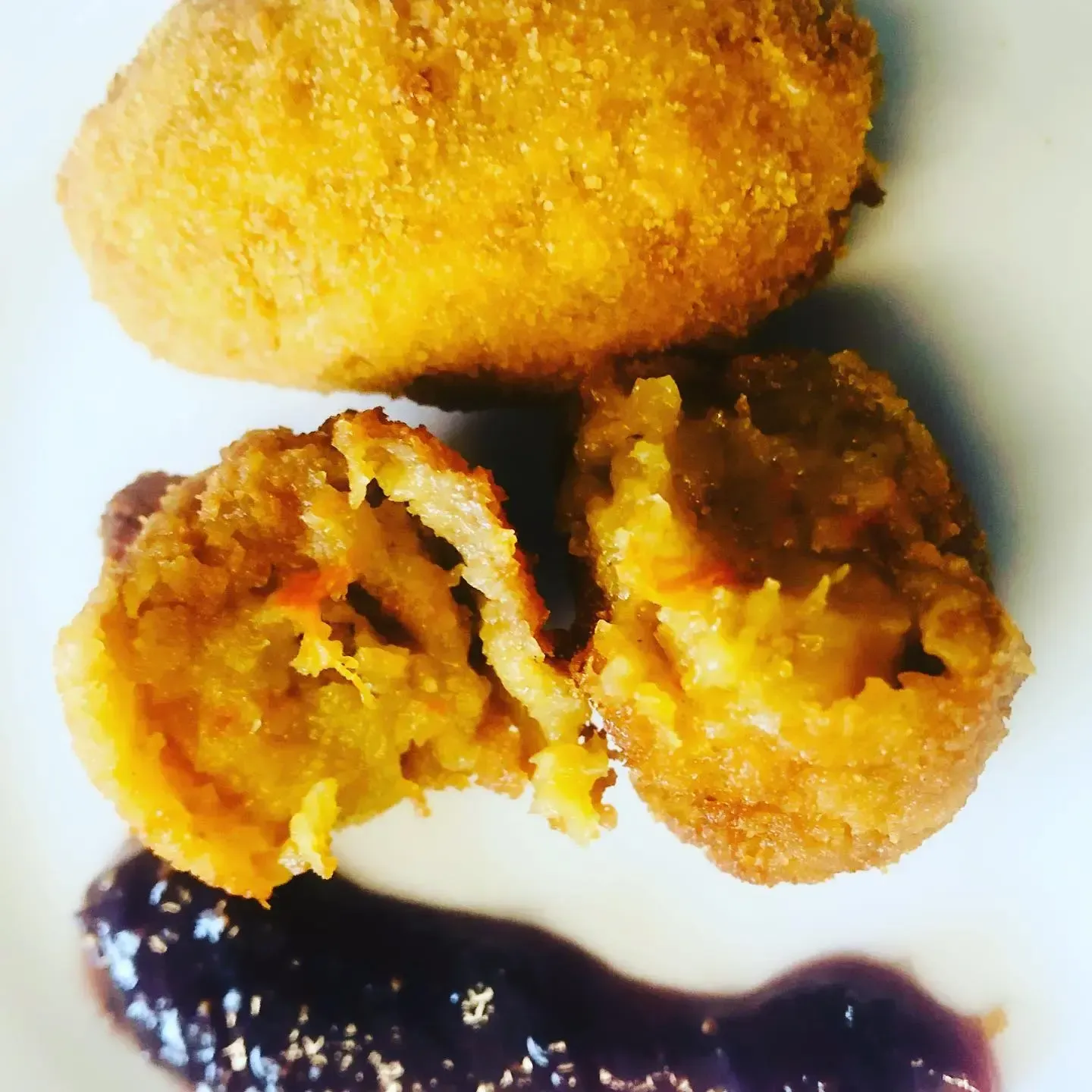 Croquetas empanizadas fritas, una de ellas cortada por la mitad, servidas en un plato con salsa oscura.
