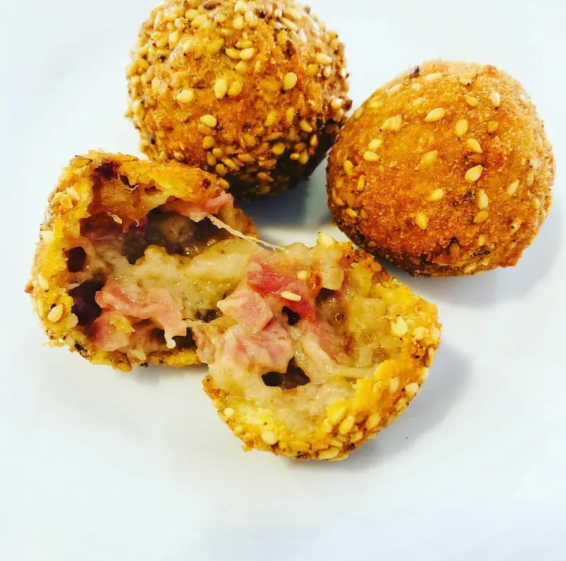 Tres bolitas rellenas fritas y crujientes, una de ellas cortada para mostrar el sabroso relleno.