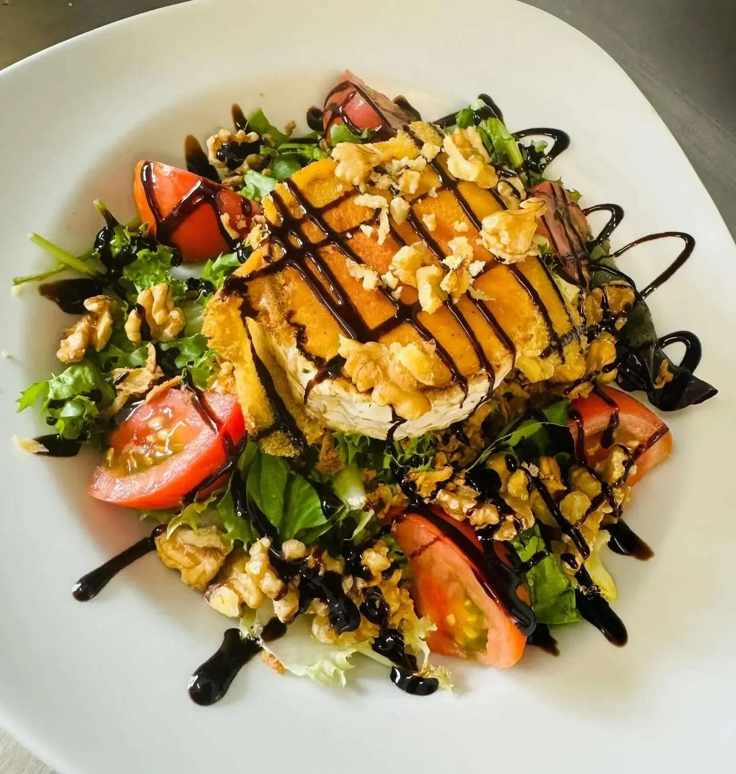 Ensalada de salmón a la parrilla con verduras, rodajas de tomate, nueces y un chorrito de vinagre balsámico en un plato blanco.