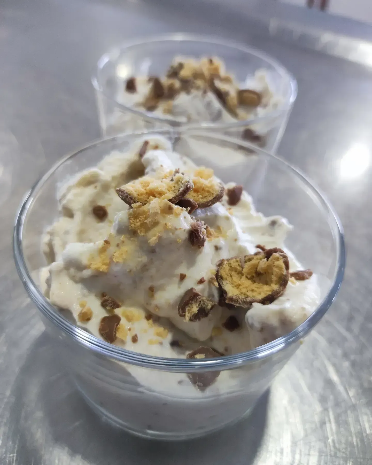 Dos vasos transparentes de postre cubiertos con crema batida y trozos de nueces sobre un mostrador de metal.