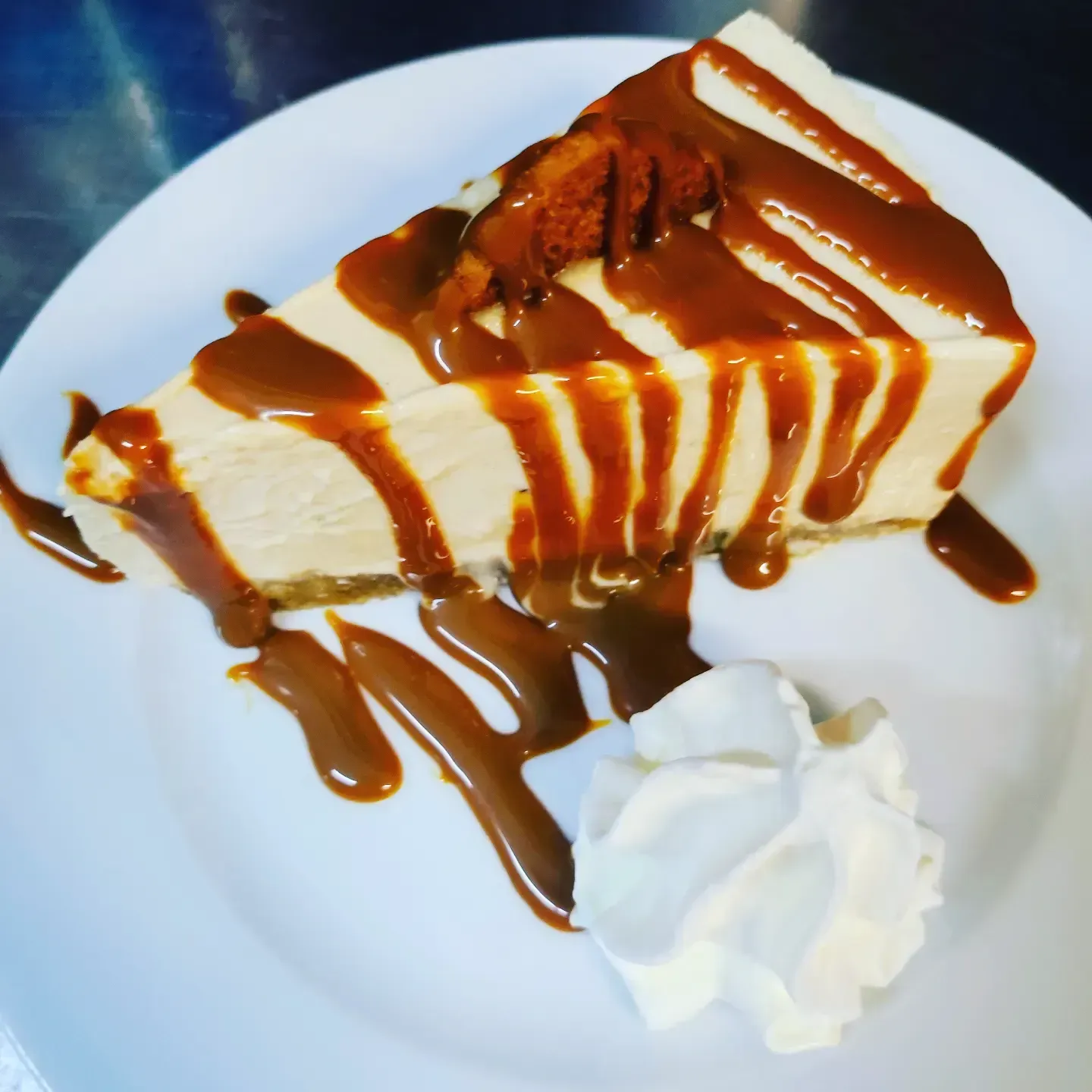 Porción de tarta de queso con sirope de caramelo en un plato blanco, cubierta con crema batida.