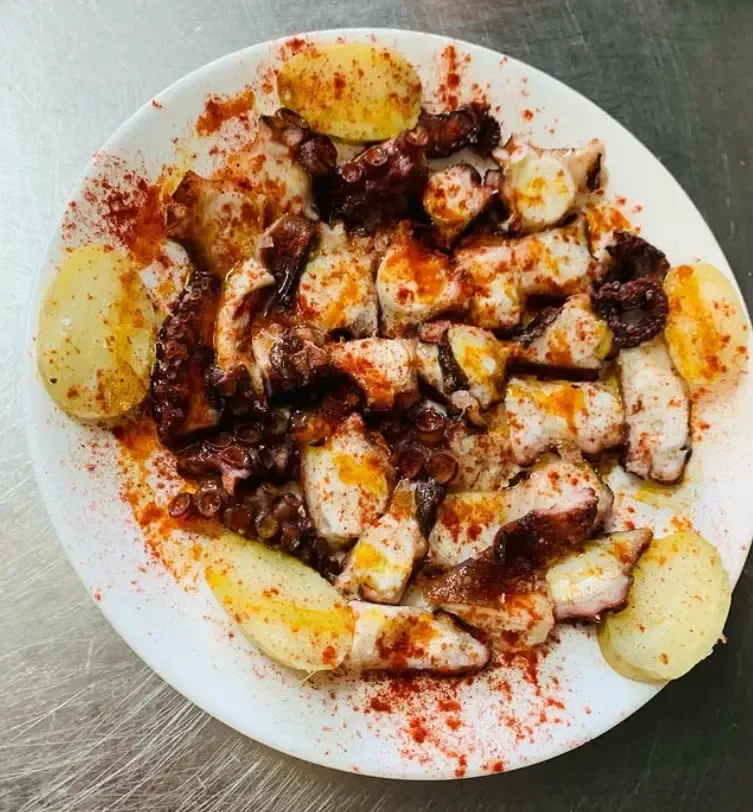 Plato de pulpo en rodajas con pimentón y patatas gajo en un plato blanco.