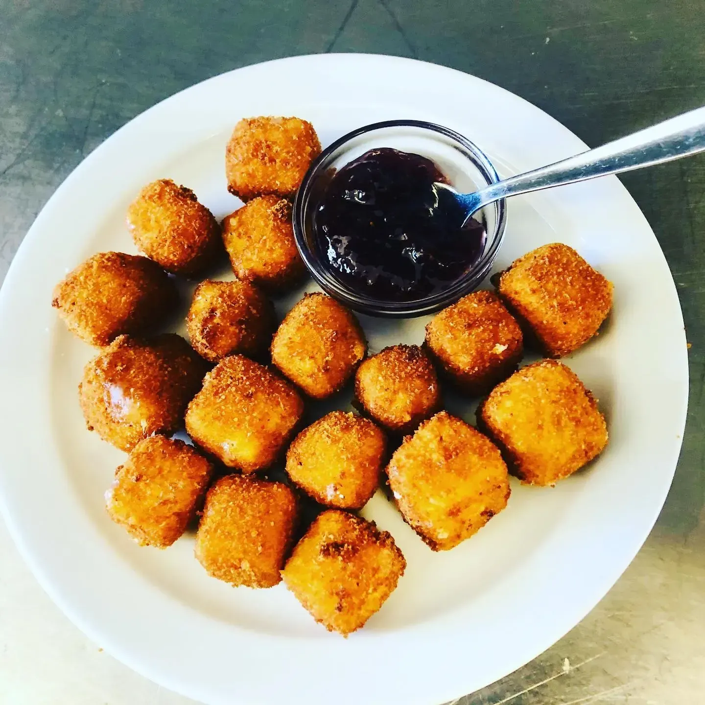 Plato de nuggets fritos dorados con un pequeño tazón de salsa oscura para mojar y una cuchara.