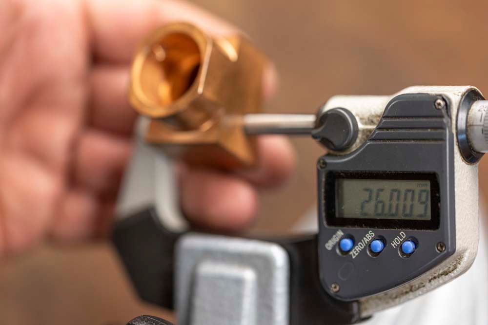 Eine Person misst ein Stück Metall mit einem digitalen Mikrometer.