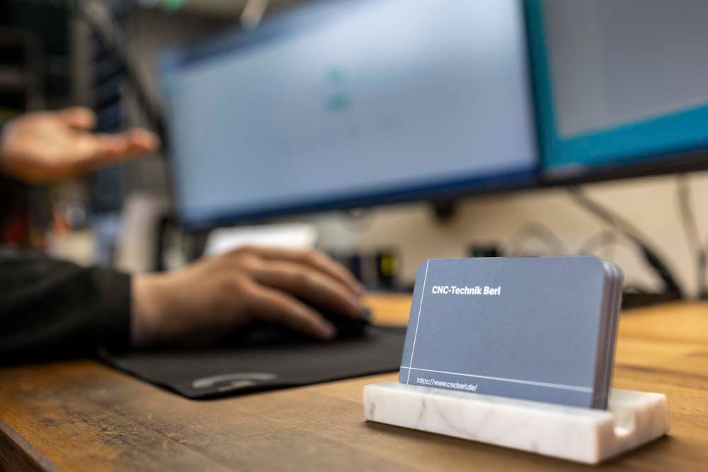 Eine Person benutzt einen Computer und auf einem Schreibtisch liegt eine Visitenkarte.