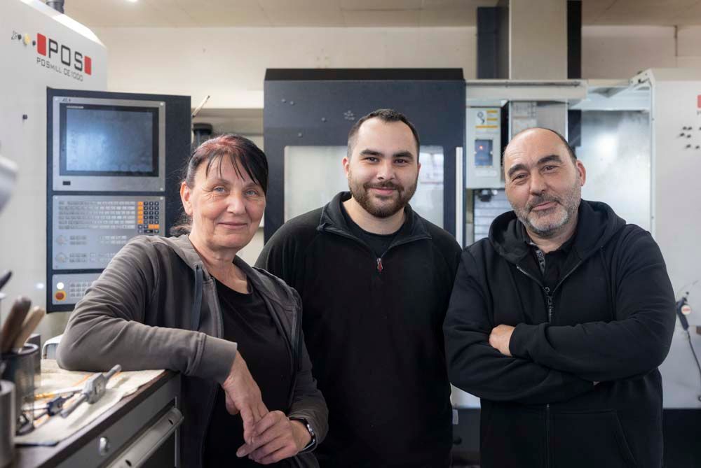 Drei Personen posieren für ein Foto vor einer Maschine in einer Fabrik.