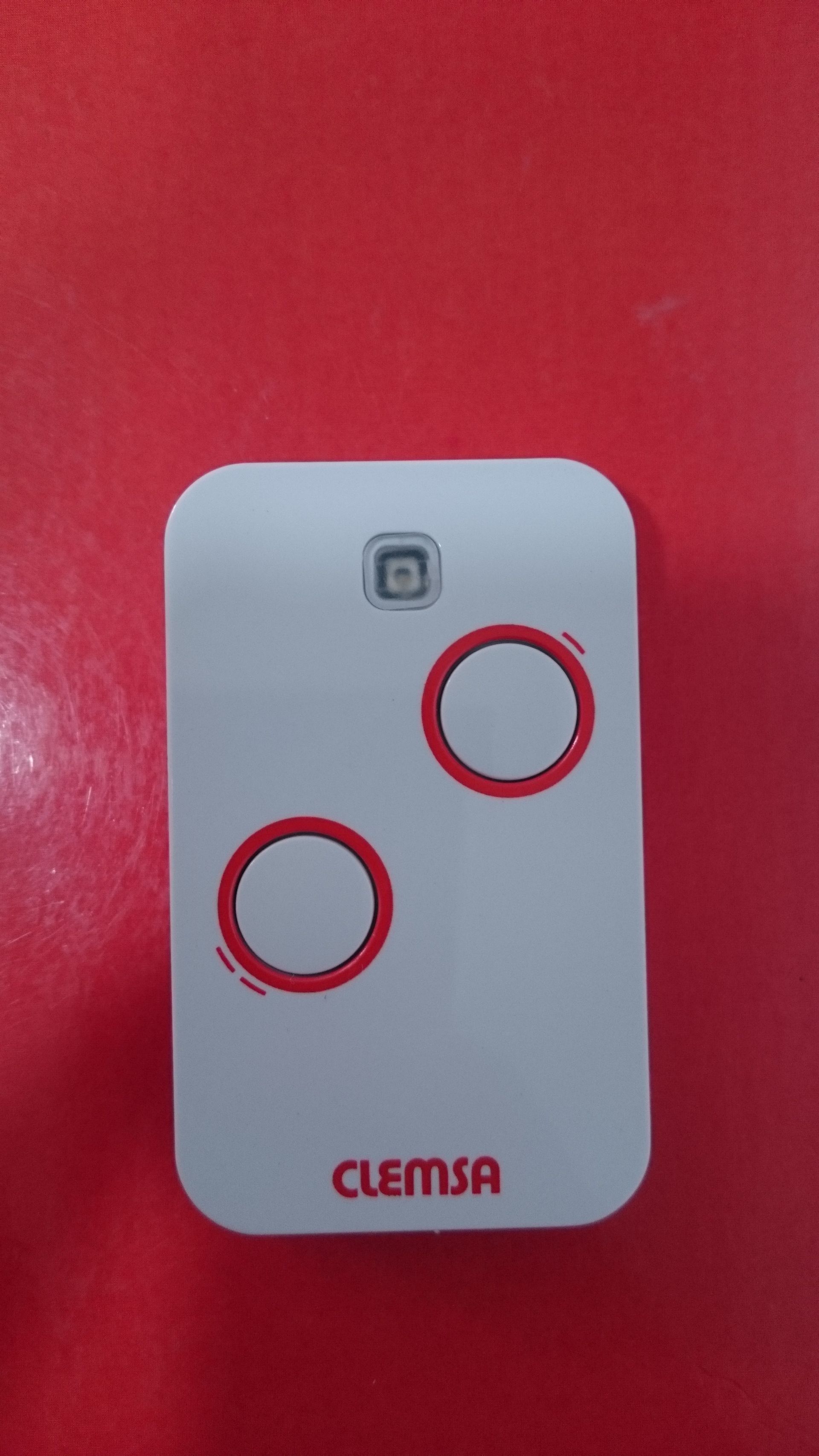 Un control remoto blanco con dos círculos rojos sobre una superficie roja.