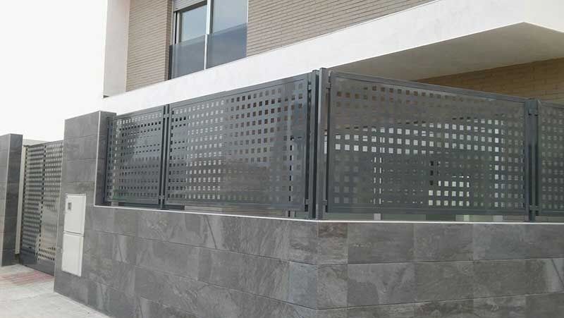 Una valla con agujeros está al lado de un edificio.