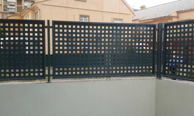 Una valla negra con agujeros está delante de un edificio.