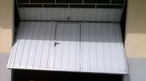 Una puerta de garaje está abierta y apoyada al costado de un edificio.