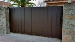 Una puerta corrediza marrón está rodeada por un muro de piedra y una palmera.