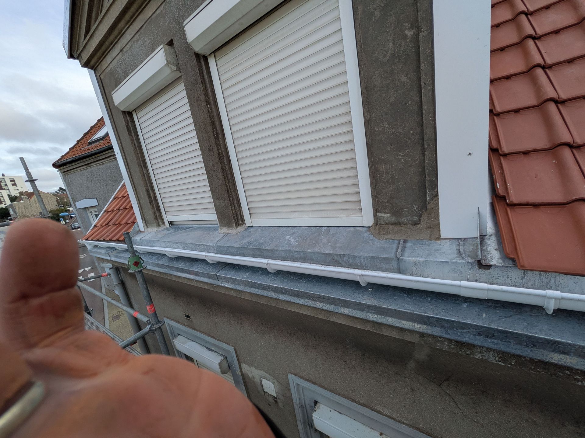 Vue rapprochée depuis un échafaudage montrant un tuyau d'évacuation blanc installé contre la façade d'un bâtiment.