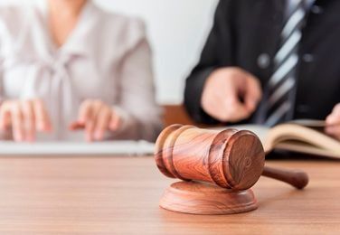 Mazo de madera sobre un escritorio, con dos personas al fondo desenfocado.