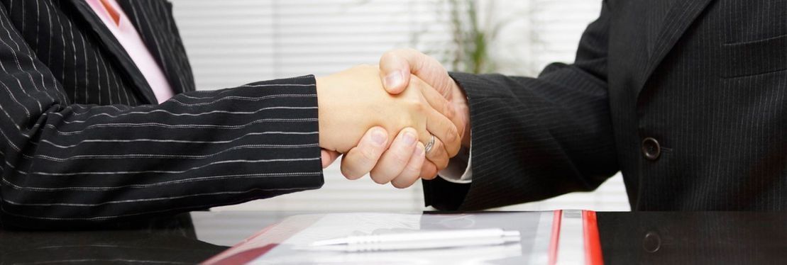 Dos personas con traje se dan la mano sobre una mesa.