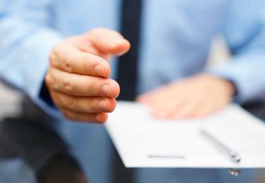 Persona con camisa azul extiende la mano hacia un documento con un bolígrafo.