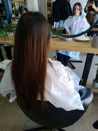 Una mujer está sentada en una silla frente a un espejo en una peluquería.