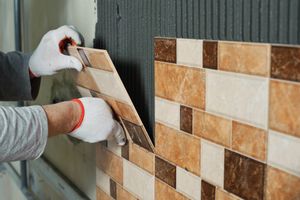 Handwerker bringt braune Mosaikfliesen an der Wand an