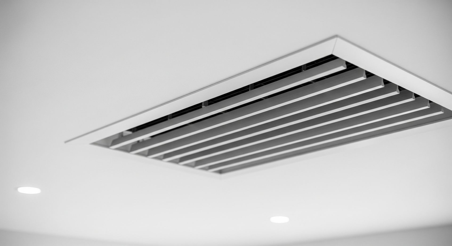 Grille d'aération encastrée dans un plafond blanc.