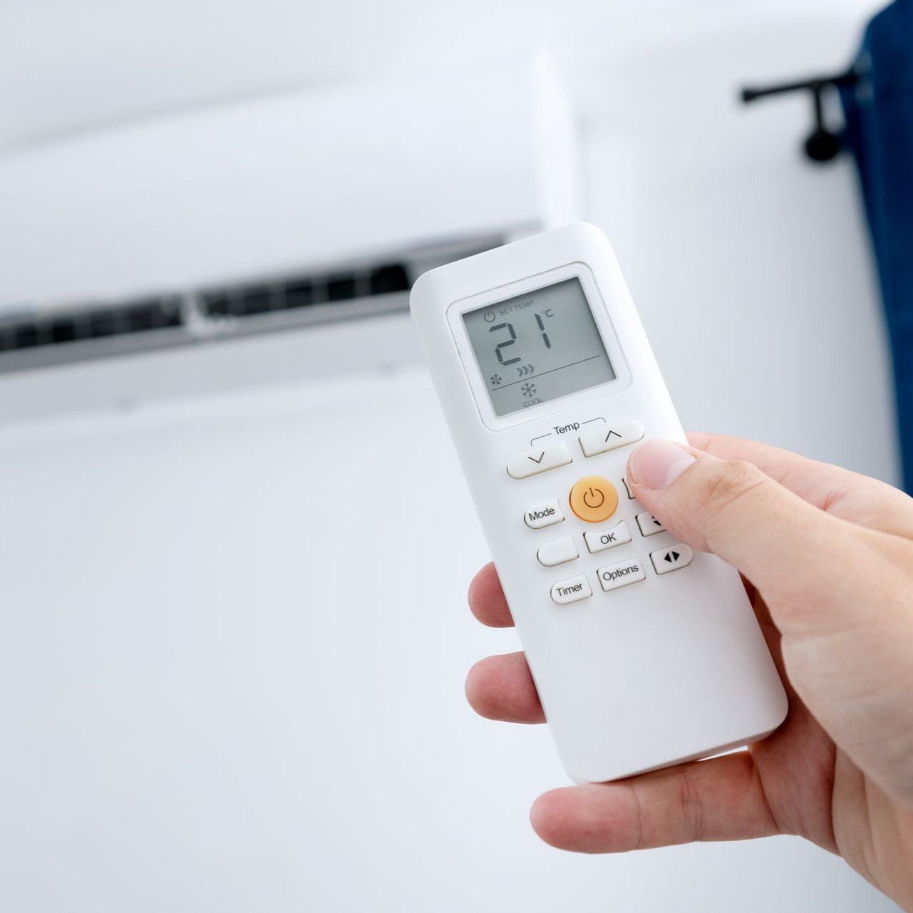 Une télécommande blanche affichant 21 °C près d'un climatiseur.