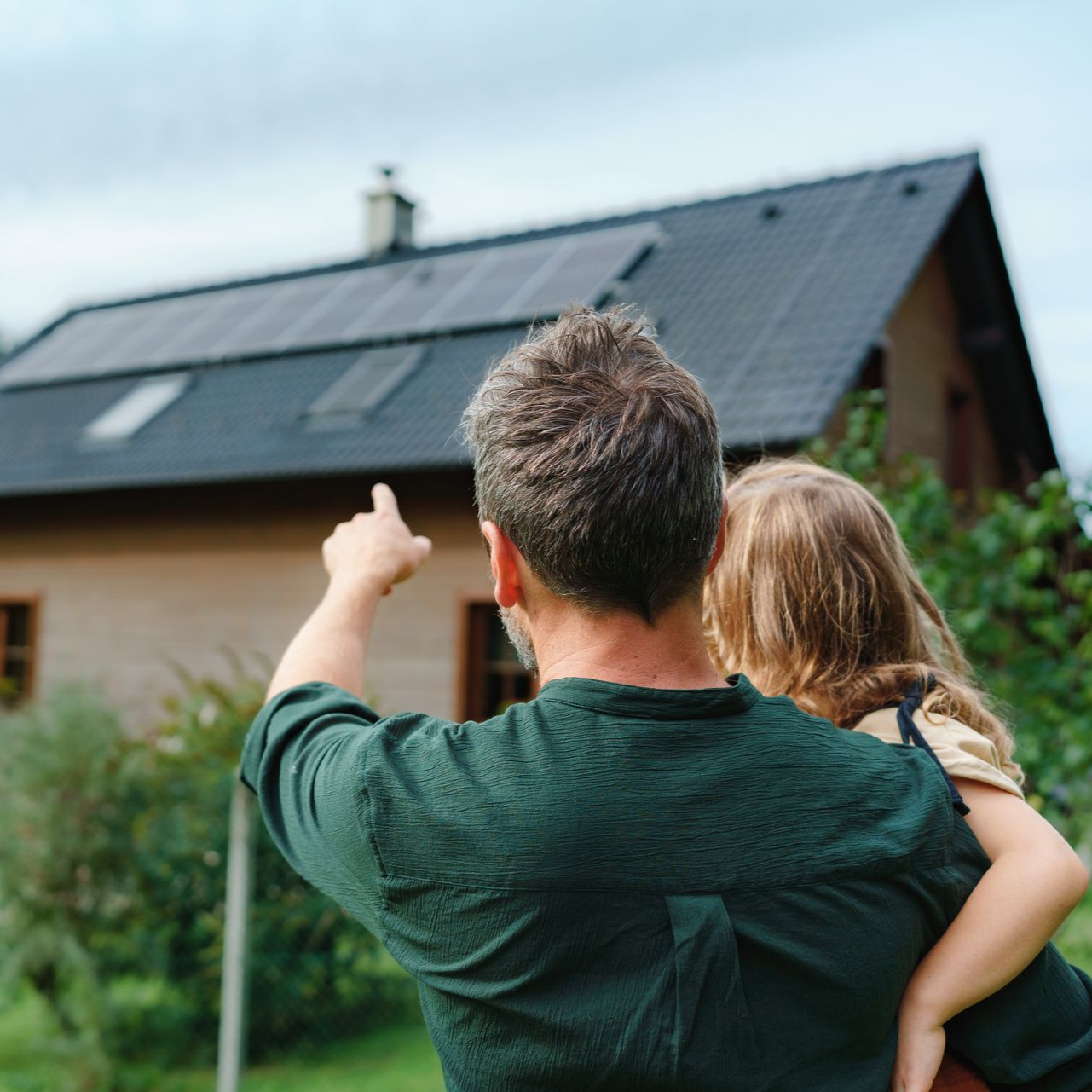 Un couple près d'une maison, pointant du doigt un ensemble de panneaux solaires sur le toit.