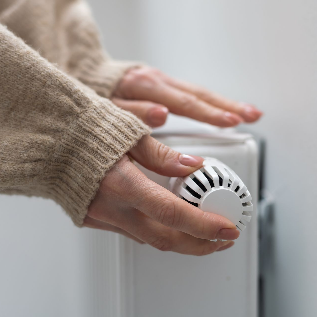 Mains ajustant le bouton du thermostat d'un radiateur.