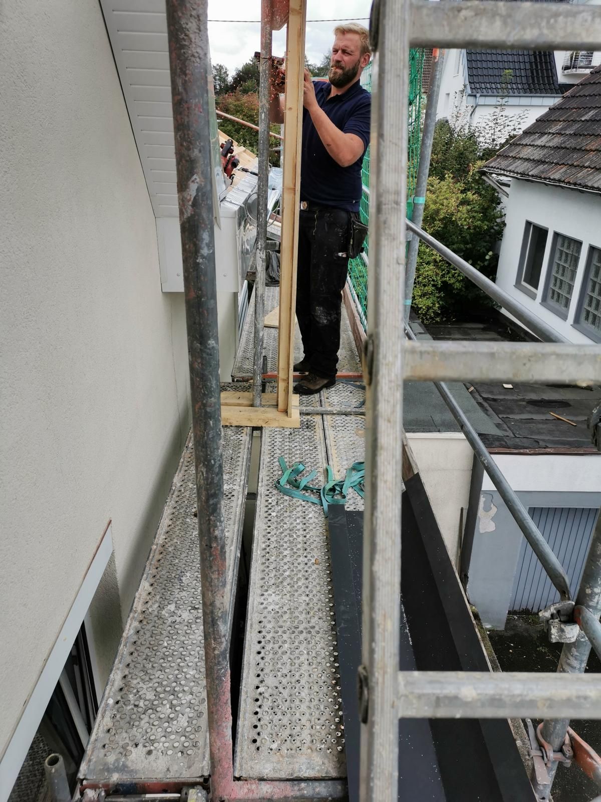 Mann auf einem Gerüst installiert Holzverkleidungen an der Außenseite eines Gebäudes.