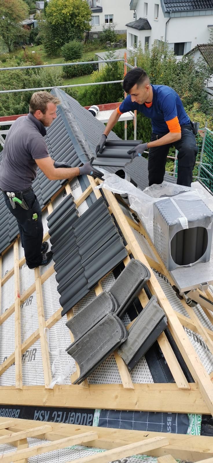 Zwei Dachdecker verlegen Ziegel auf einem Dach; im Freien in einem Wohngebiet.