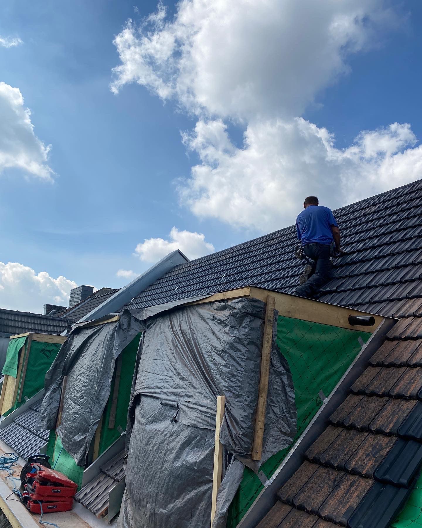 Dachdecker arbeitet an einem neuen Dach mit schwarzen Ziegeln unter einem teilweise bewölkten blauen Himmel.