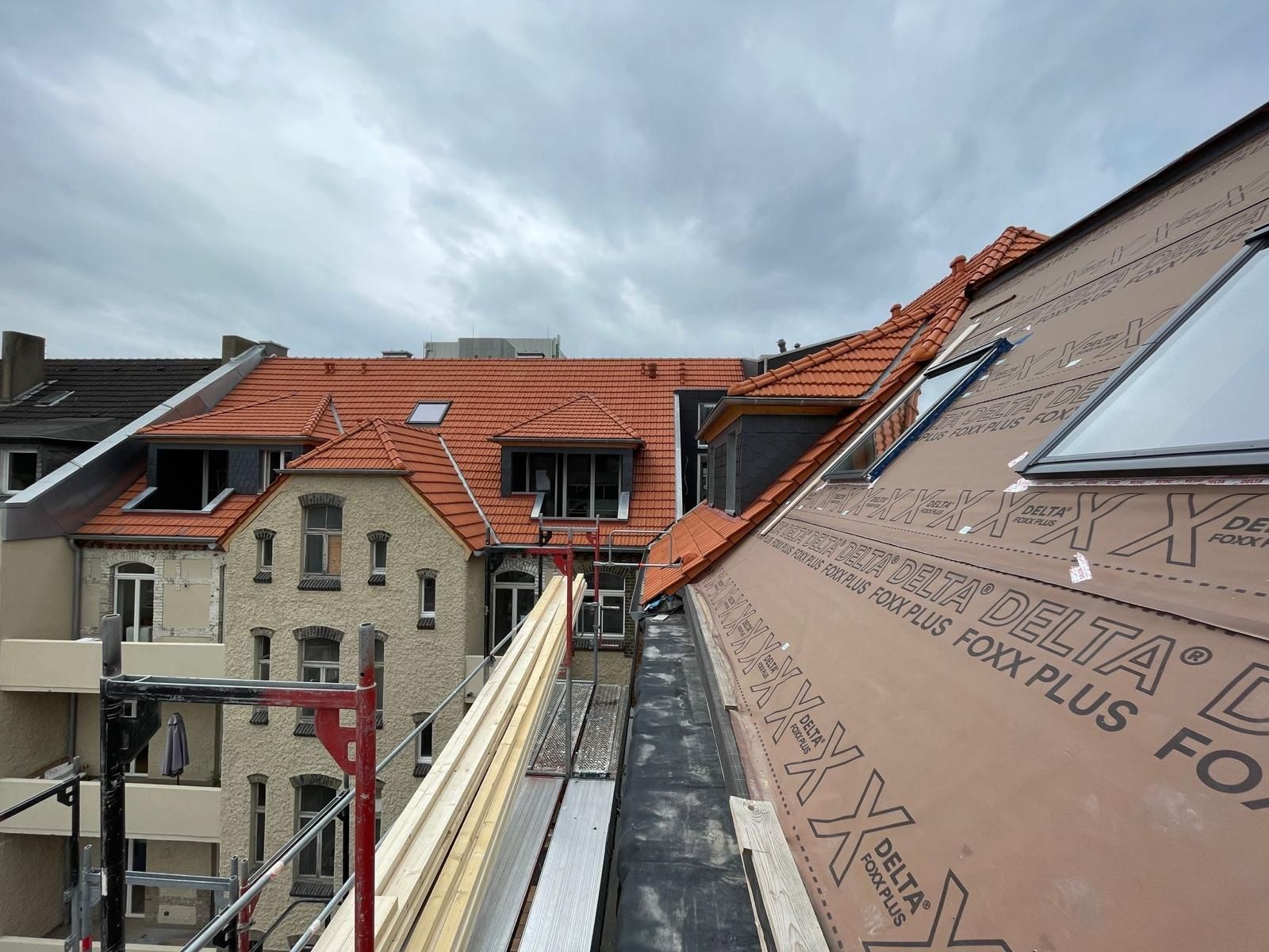 Dachkonstruktion mit rotem Ziegeldach, freiliegender Isolierung und Dachgaubenfenstern an einem bewölkten Tag.