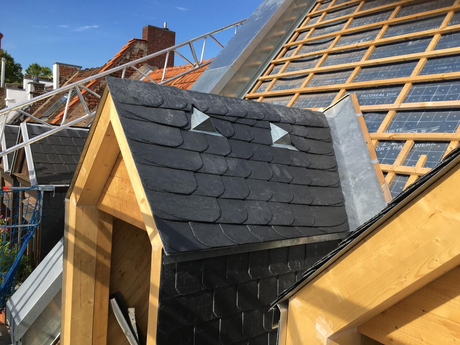 Dacharbeiten im Gange: Schieferziegel auf einem Dachfenster, Holzrahmen, blauer Himmel.