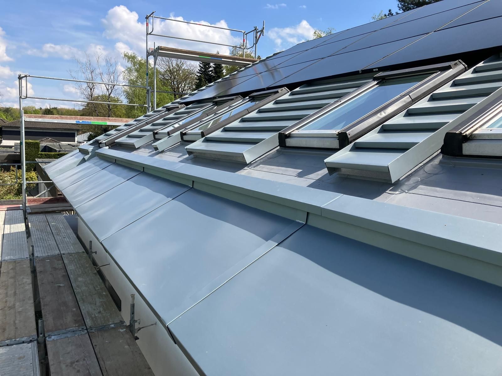 Ein graues Metalldach mit Oberlichtern, aus einem niedrigen Winkel betrachtet, im Hintergrund ein Gerüst.