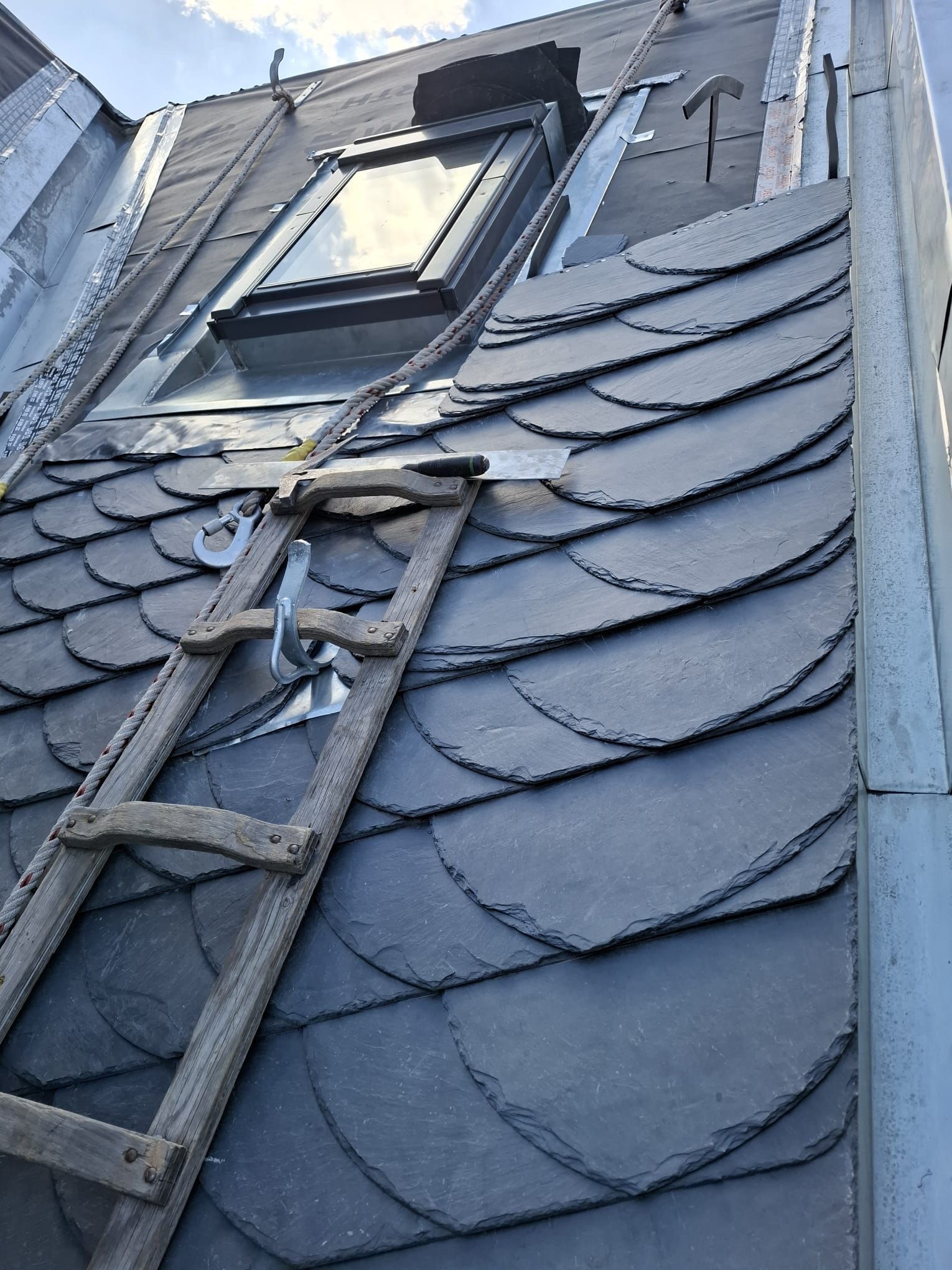 Leiter auf einem Schieferdach, in der Nähe eines Oberlichts. Graue Schieferziegel.