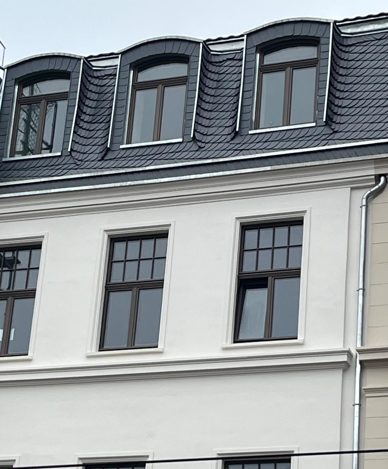 Weißes Gebäude mit dunklem Dach und dunklen Fenstern; einige Dachgauben.