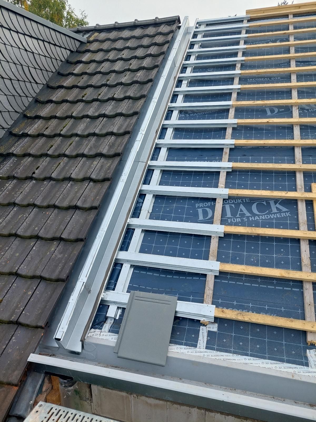 Dach mit Ziegeln, freiliegenden Dachsparren und Metallverkleidung während der Bauphase.