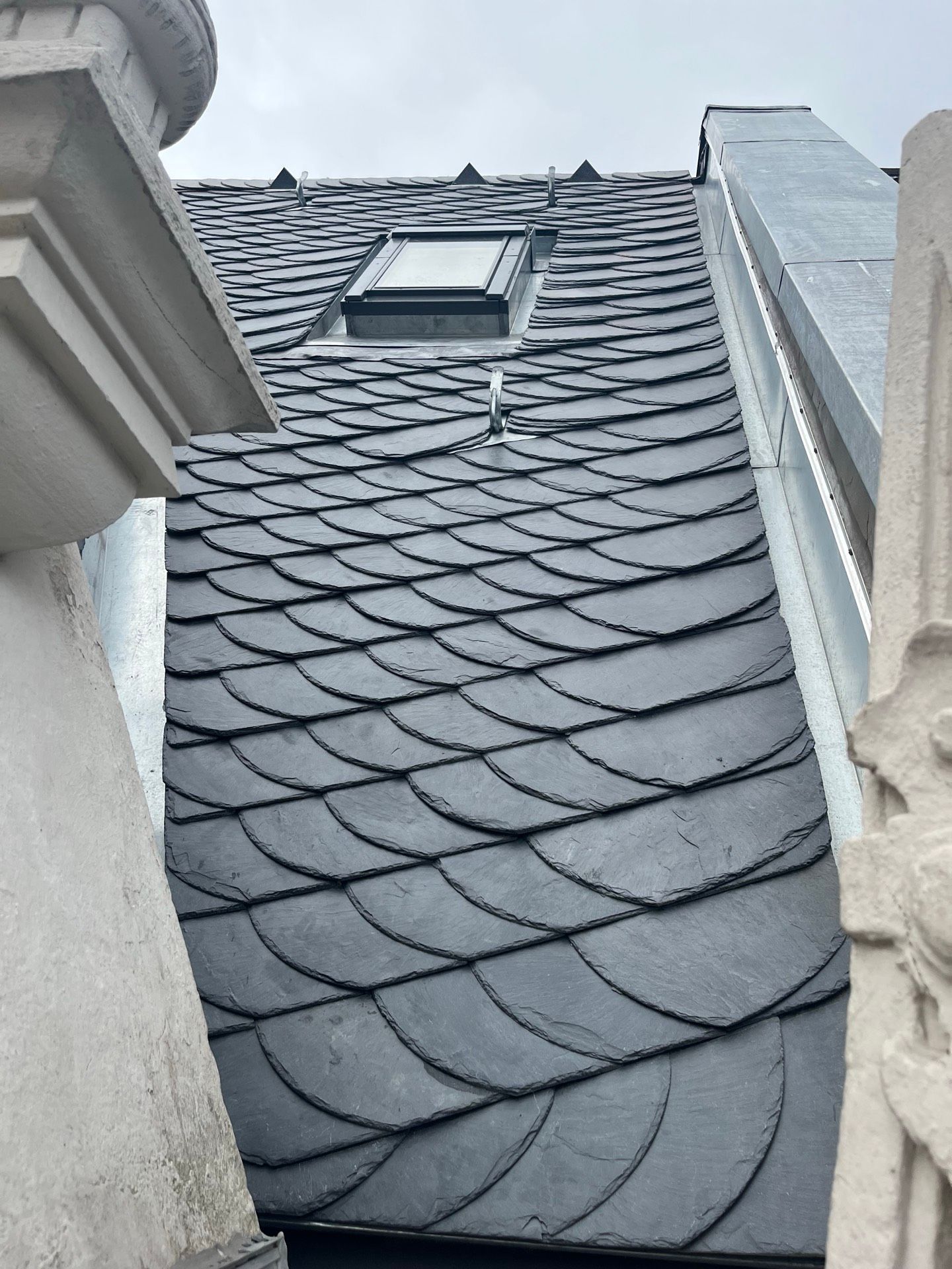 Dunkles Schieferdach mit gewölbten Ziegeln, einem kleinen Oberlicht und architektonischen Details.