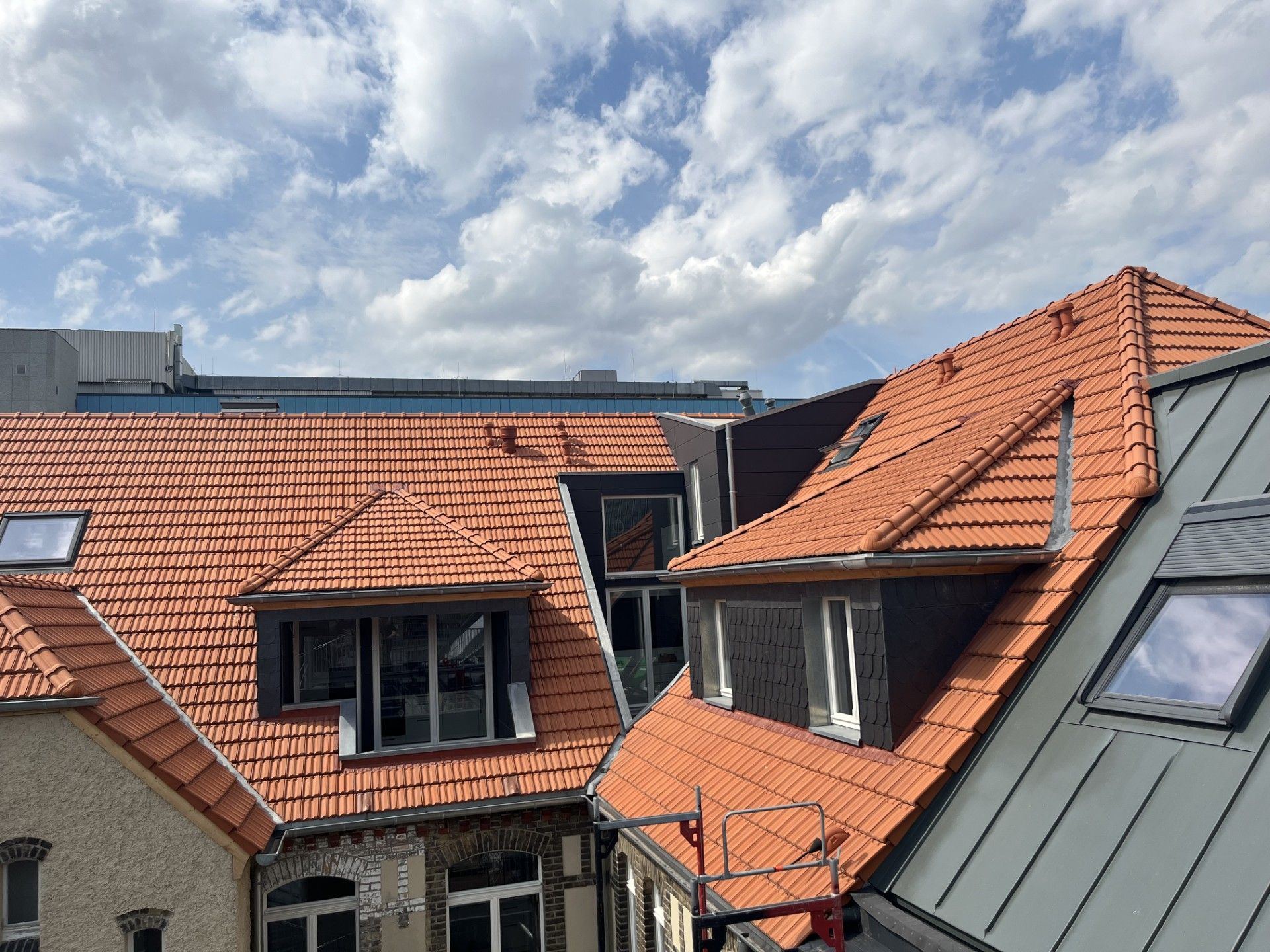 Dächer von Gebäuden mit orangefarbenen Ziegeln vor einem bewölkten blauen Himmel.