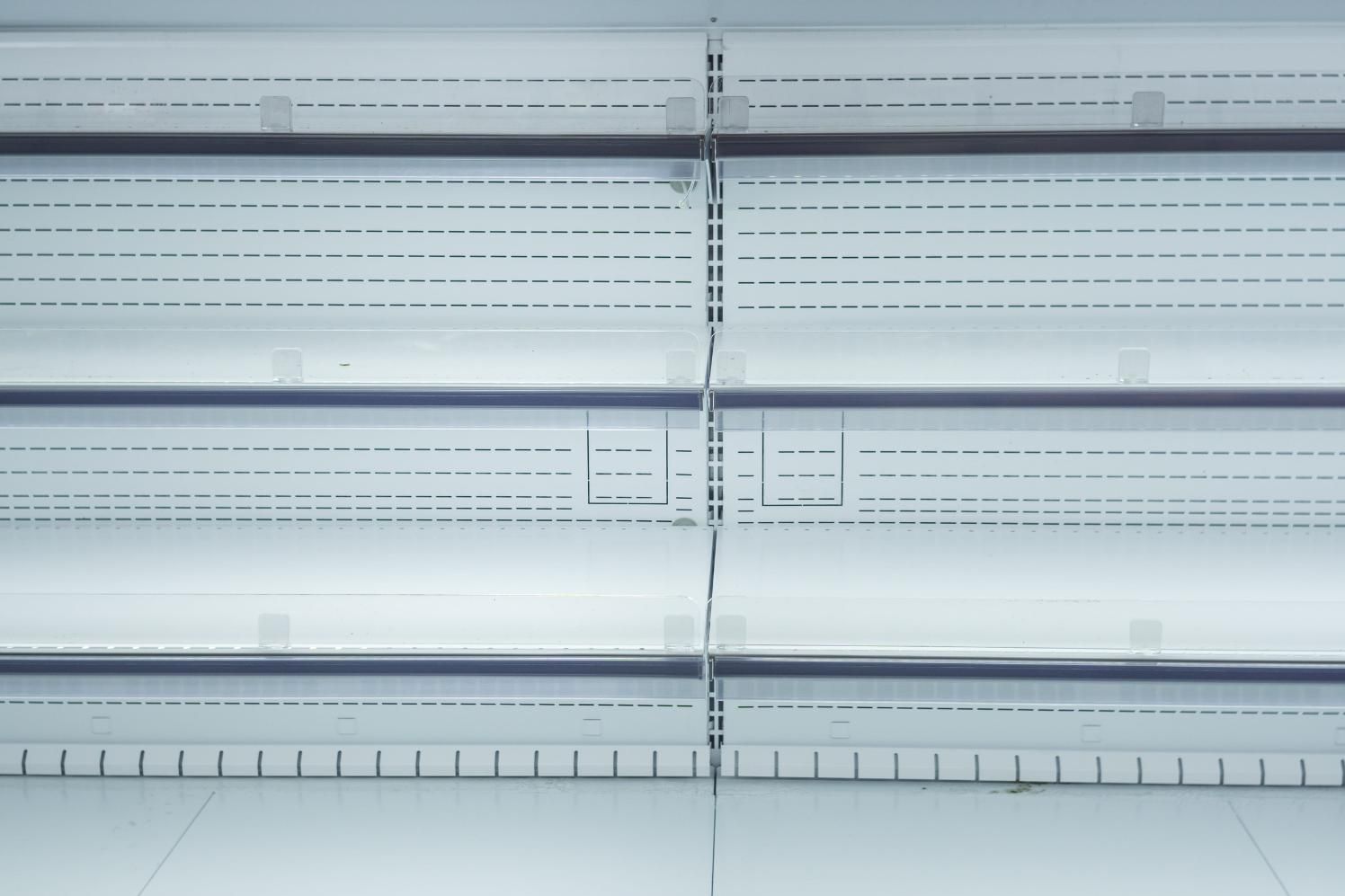 Estantes refrigerados vacíos en un supermercado, con separadores de plástico transparente y rieles para indicar el precio.