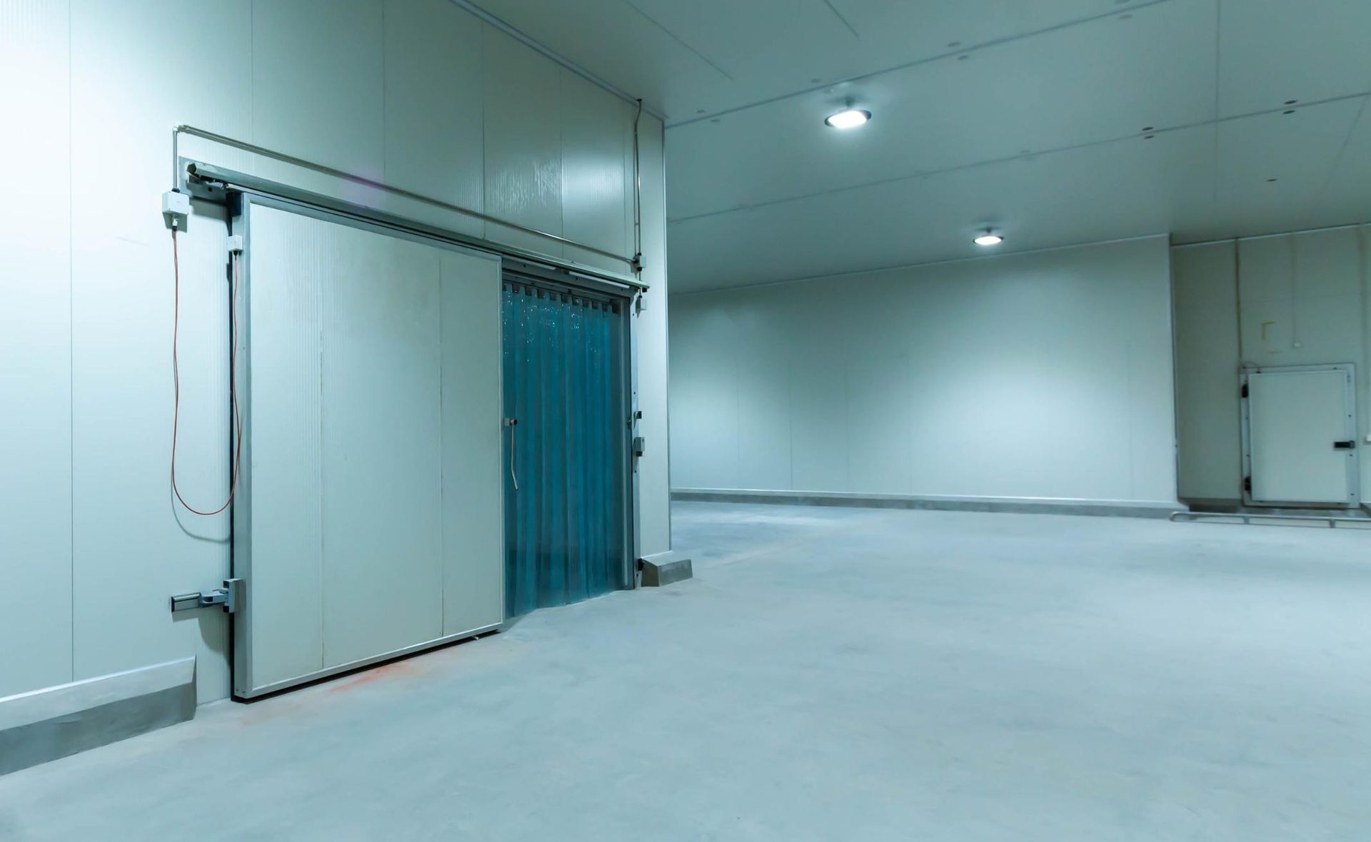 Habitación industrial vacía con paredes blancas, puerta corredera azul y suelo de hormigón liso.