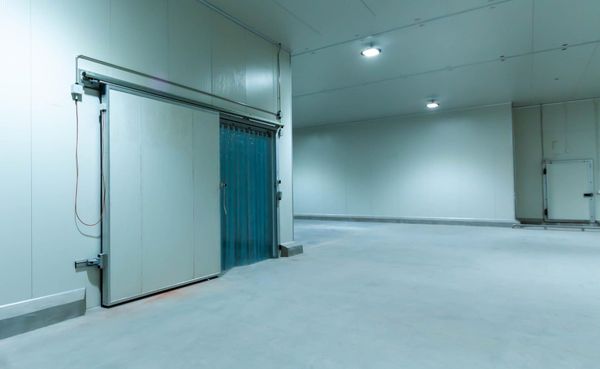 Habitación industrial vacía con paredes blancas, puerta corredera azul y suelo de hormigón liso.