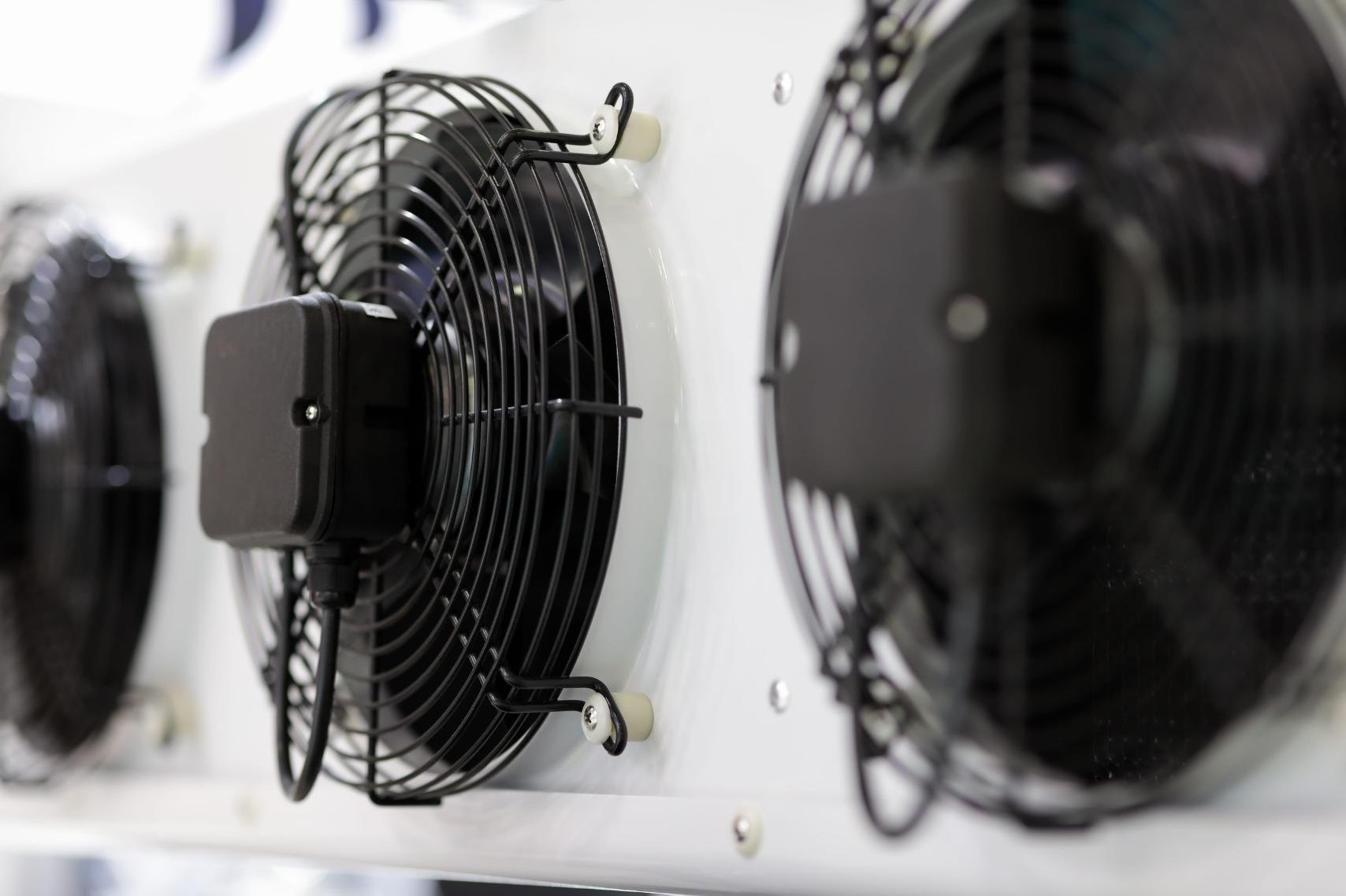 Fila de ventiladores negros montados en la pared en una habitación industrial luminosa.