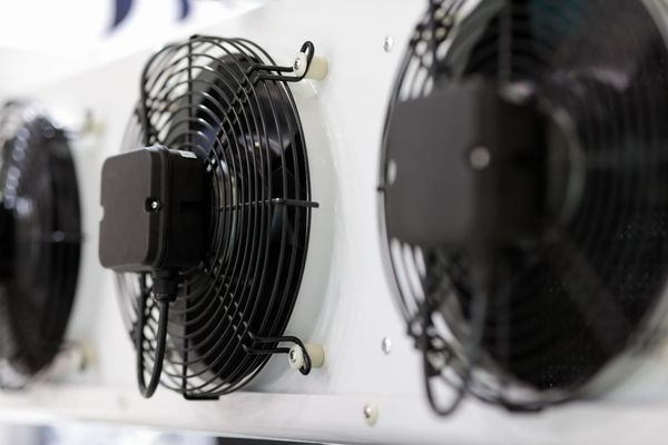Fila de ventiladores negros montados en la pared en una habitación industrial luminosa.