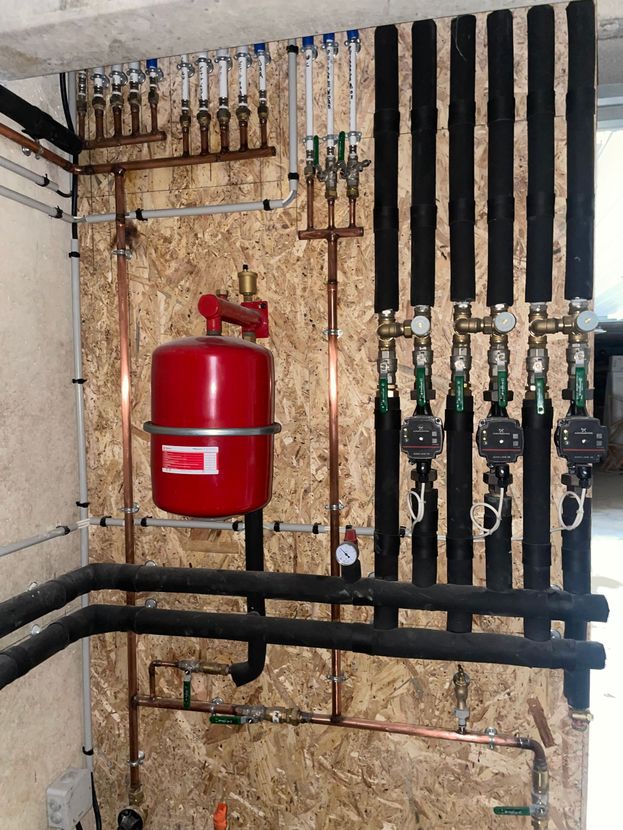 Système de chauffage avec tuyaux en cuivre, vase d'expansion rouge et tuyaux isolés noirs.