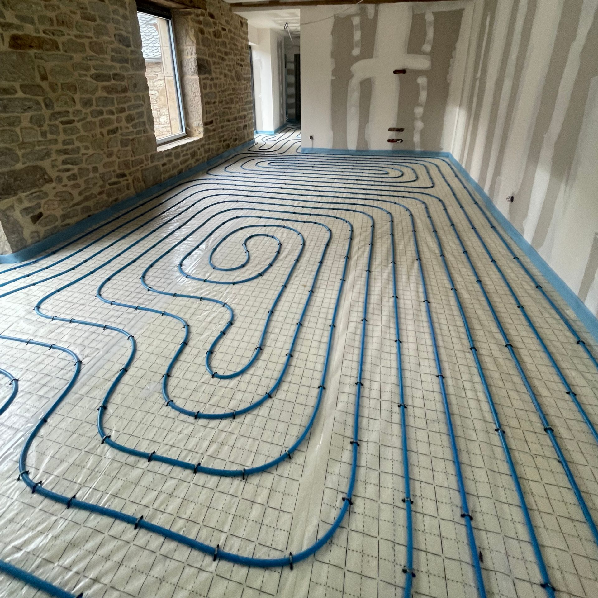 Installation d'un système de chauffage au sol : tuyauterie posée sur un sol et reliée à un collecteur par des tuyaux.