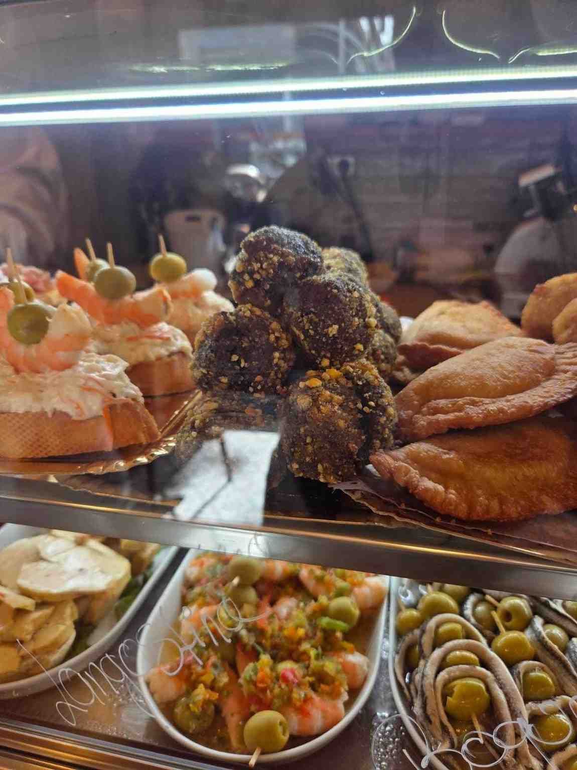 Vitrina de tapas variadas: entrantes de gambas, croquetas, empanadas y aceitunas.