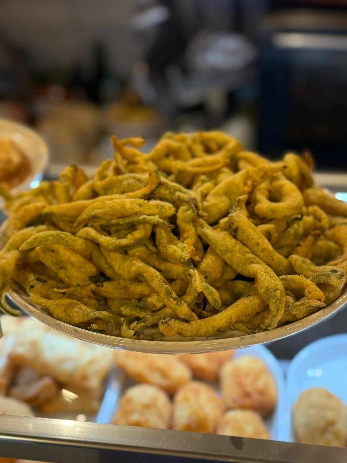 Pimientos verdes fritos apilados en un plato blanco, entorno de restaurante.