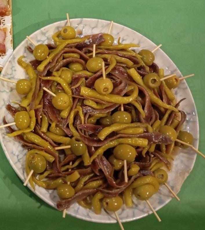 Plato de tapas españolas: anchoas, aceitunas y pimientos encurtidos en brochetas.