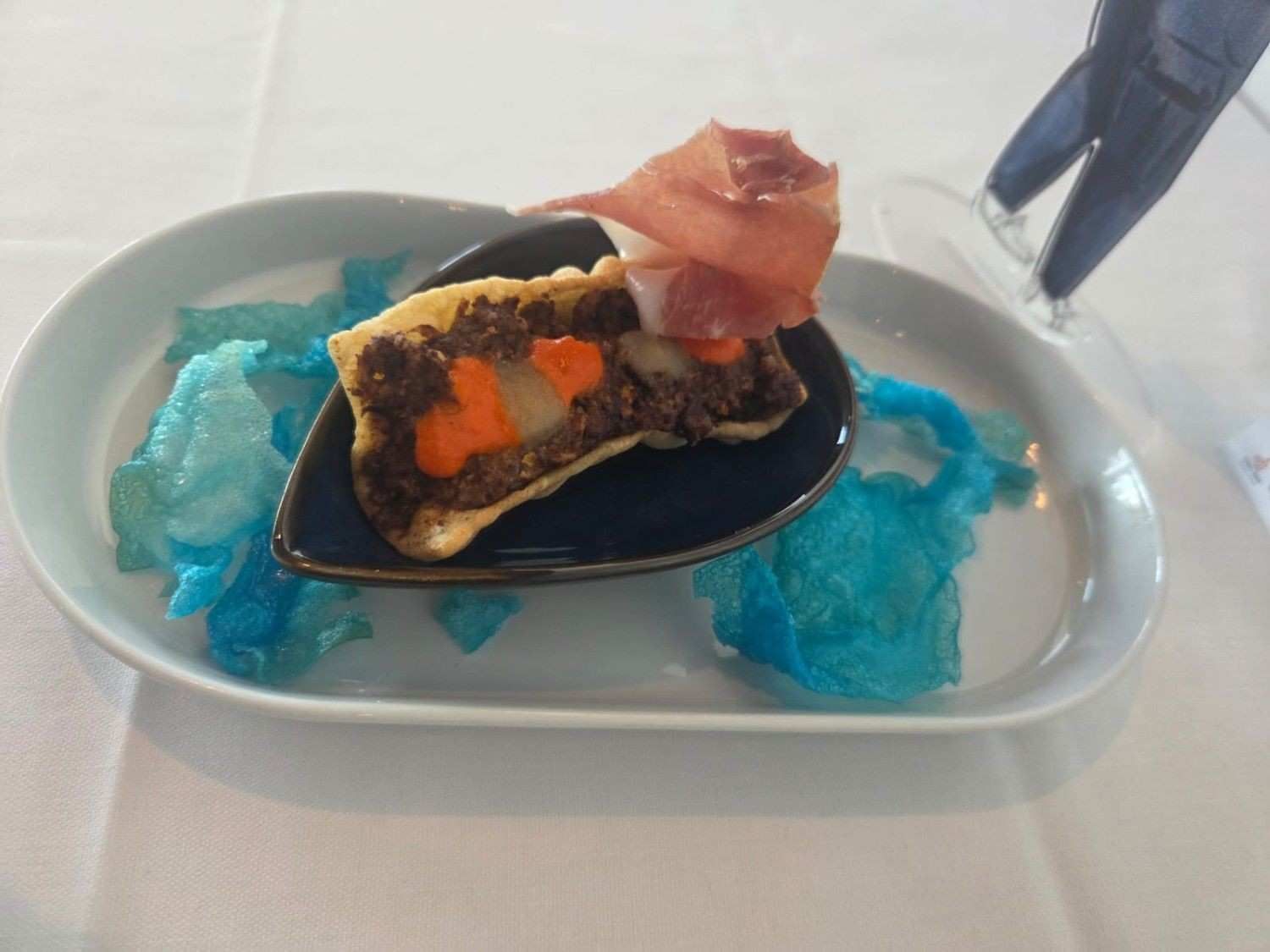 Aperitivo: pastel salado con carne, zanahorias, prosciutto y patatas fritas azules en un plato blanco.